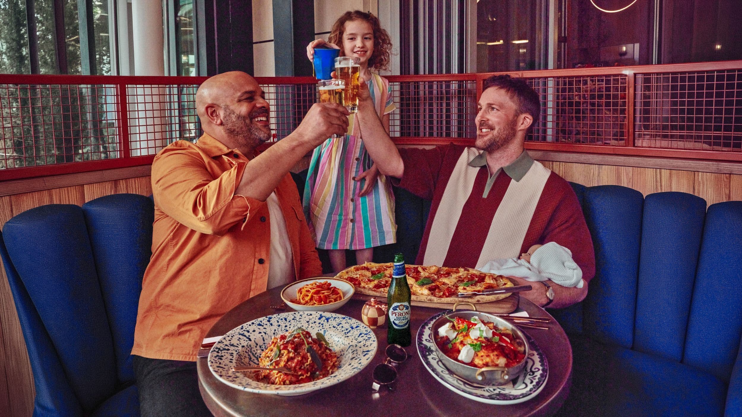 Two men and a girl toasting with drinks at a restaurant table