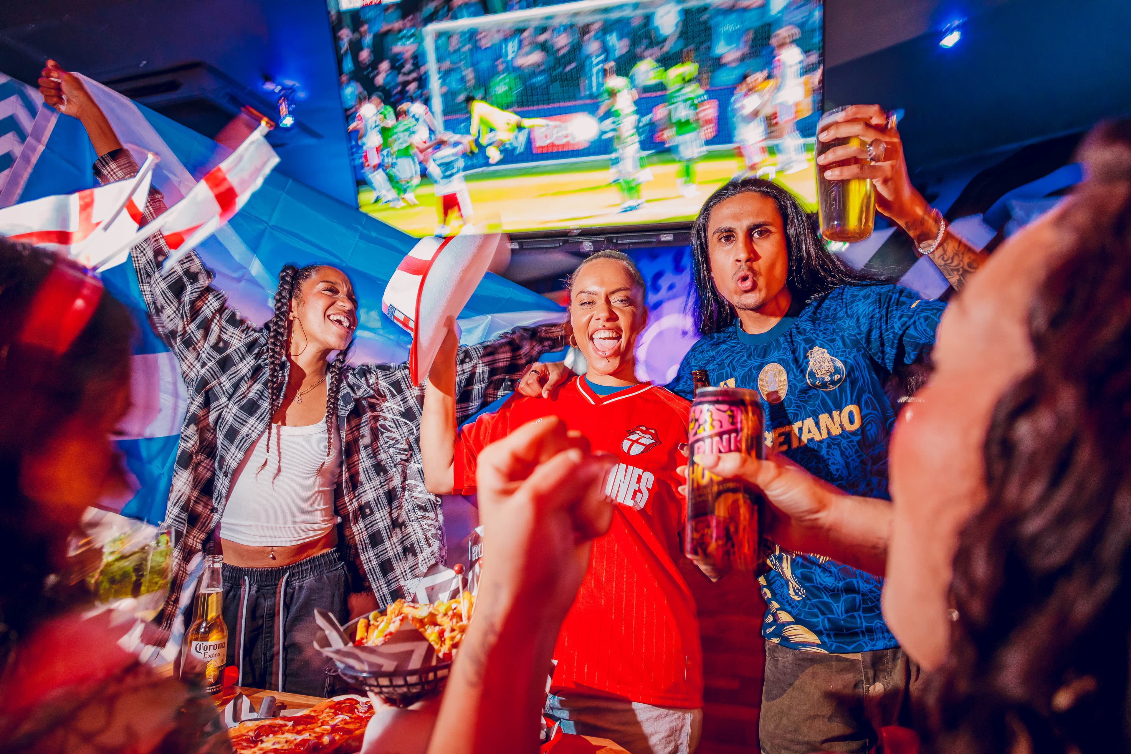 Group of friends cheering in a pub with football on TV
