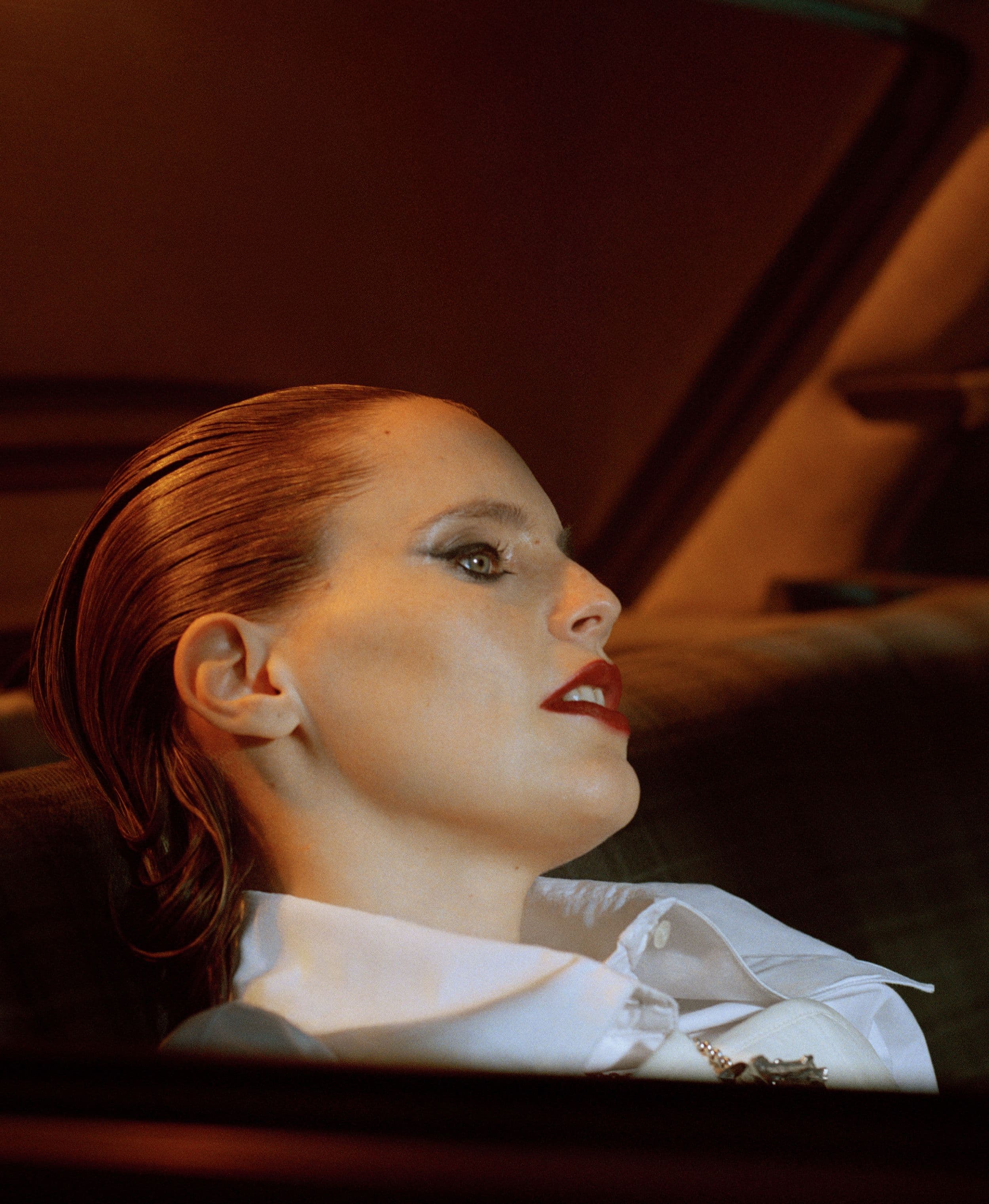 Person with slicked-back hair and white shirt in dim lighting