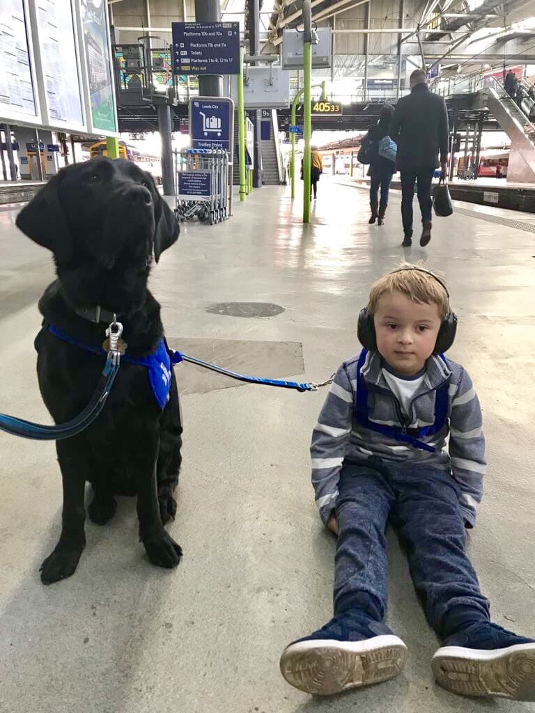 Young boy with headphones sits on train station floor with guide dog