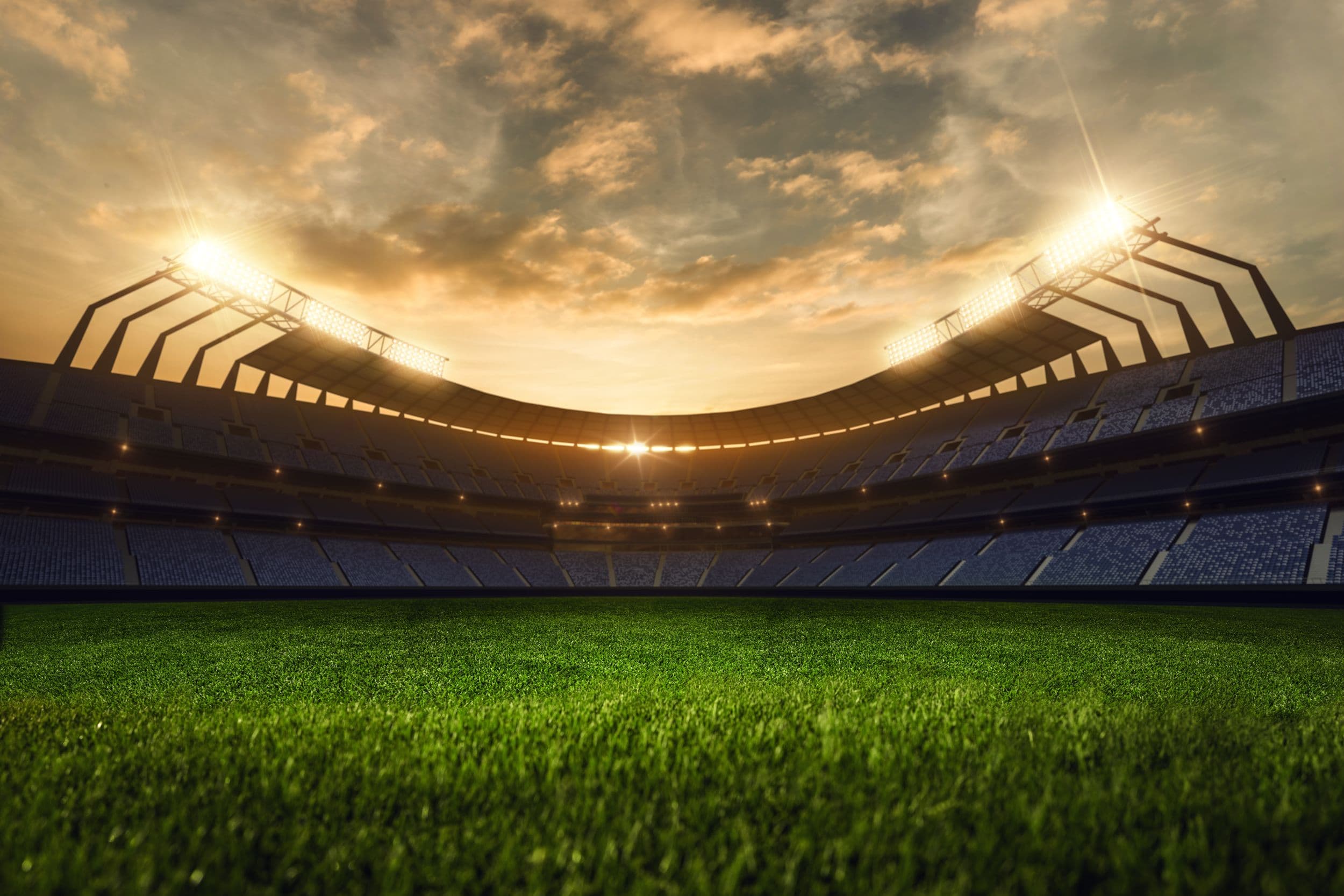 Illuminated football stadium at sunset with green field