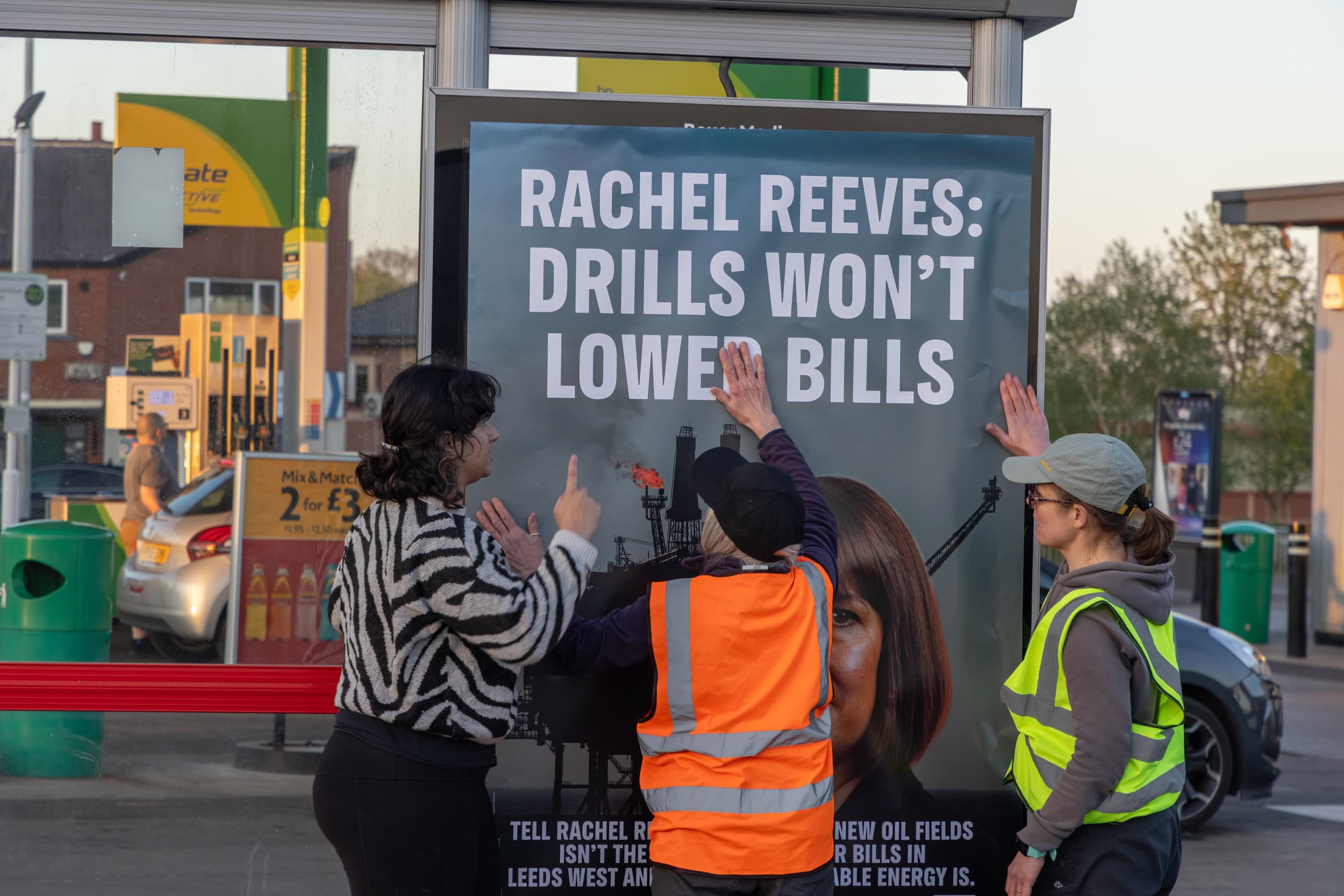 Three people examining a protest poster at a gas station