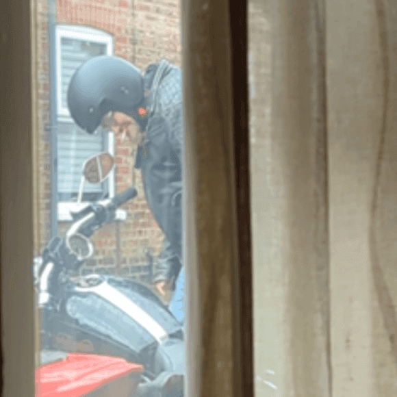 Person in black helmet beside motorcycle near brick wall