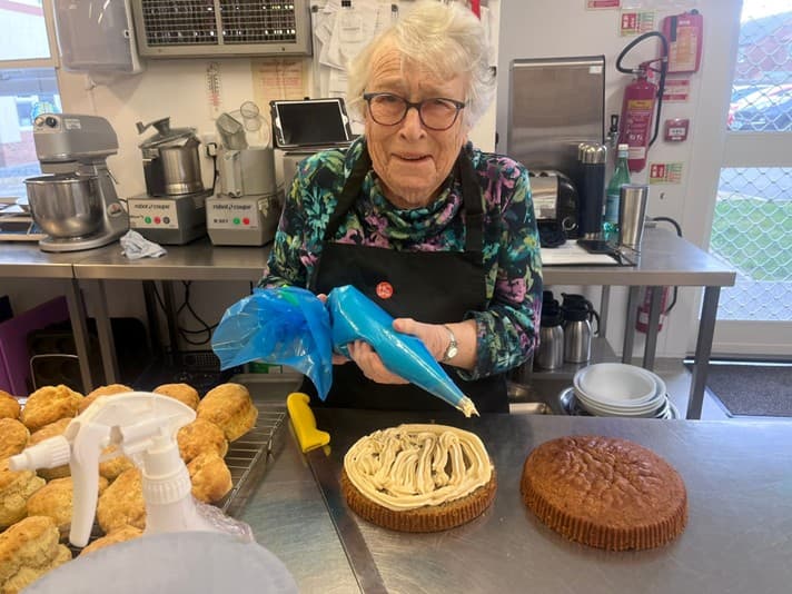 Elderly woman decorating a cake in a bakery kitchen
