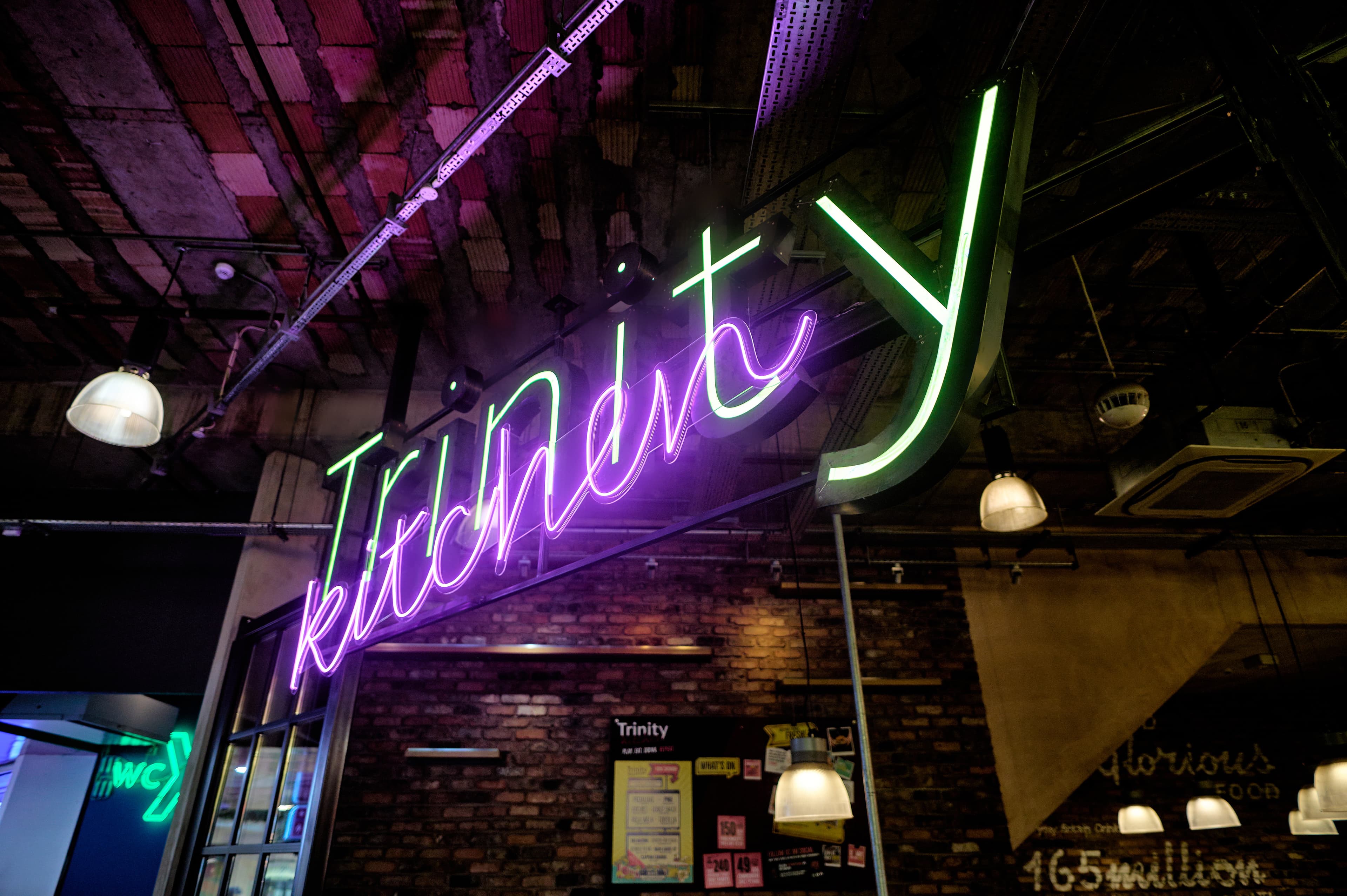 Neon sign reading 'Trinity Kitchen' on brick wall