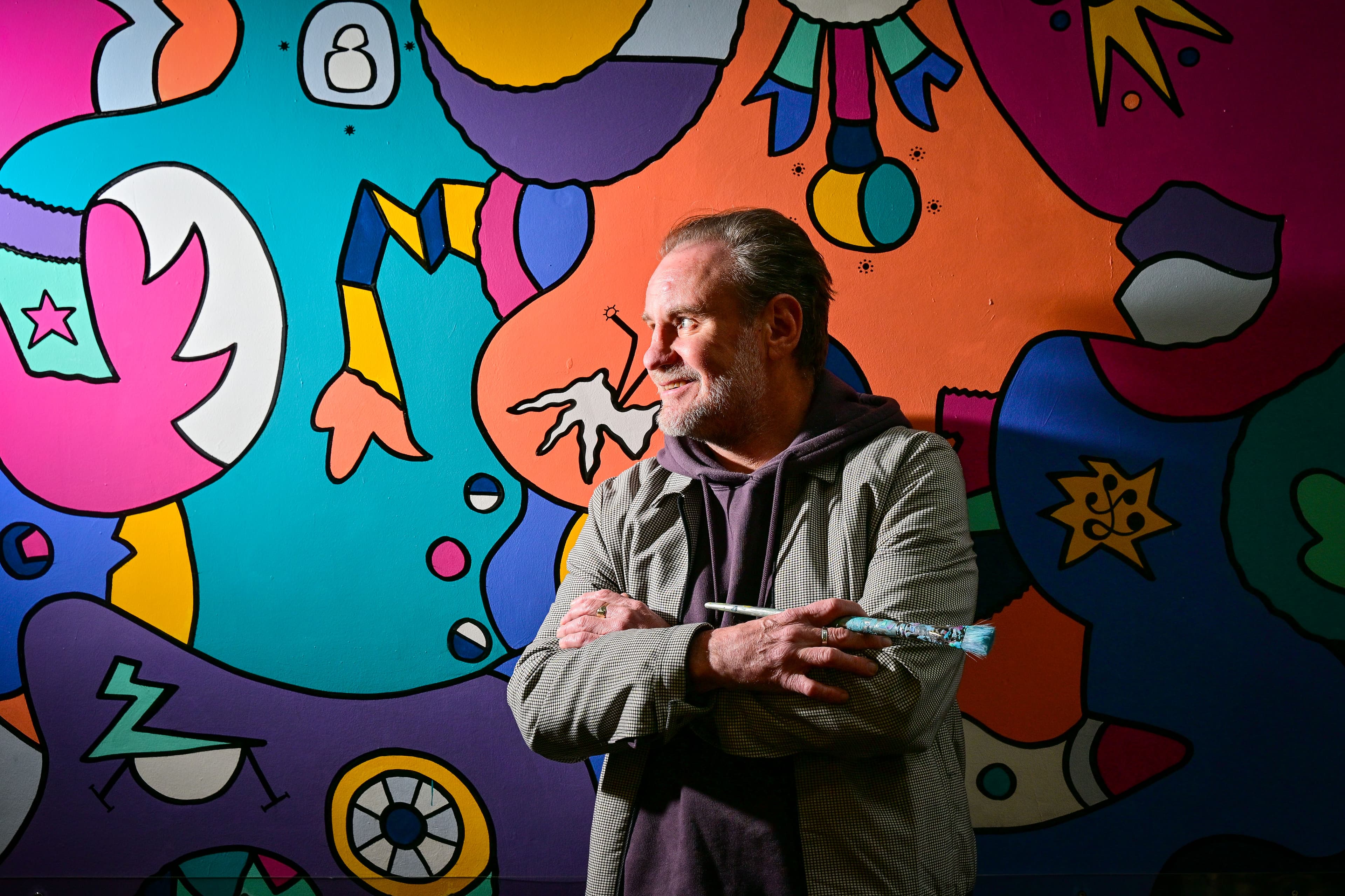 Man holding paintbrush in front of colorful abstract mural