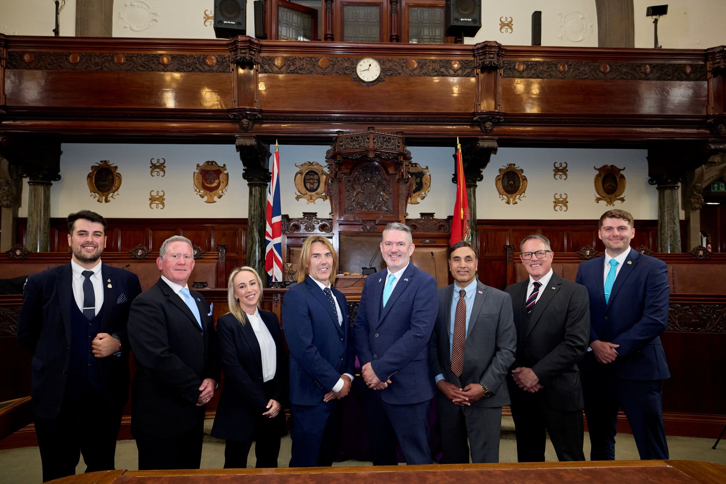 Group of eight people in formal attire inside historic chamber