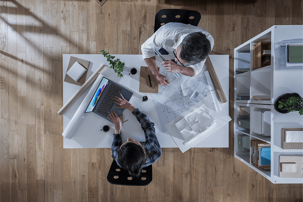 Two architects discussing blueprints at a wooden desk