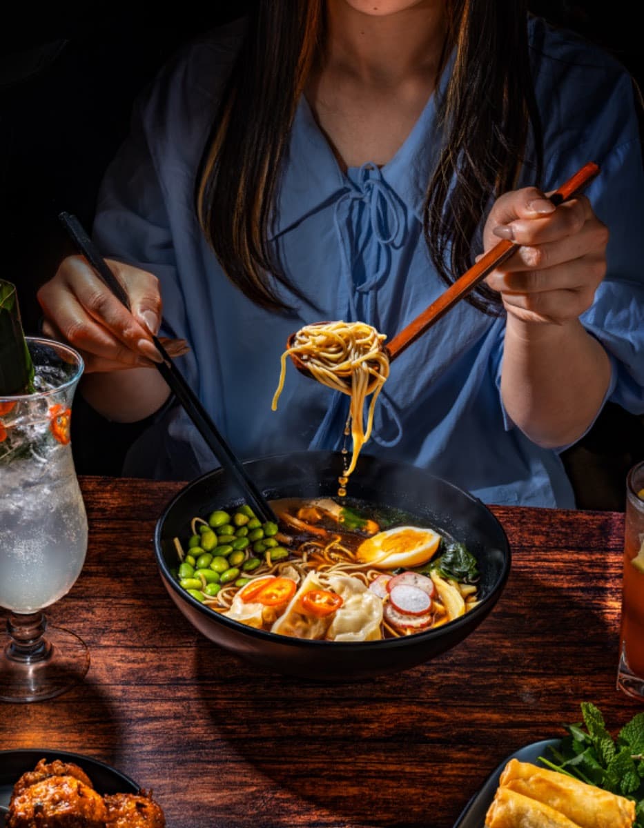Woman in blue shirt enjoying ramen with chopsticks at a table