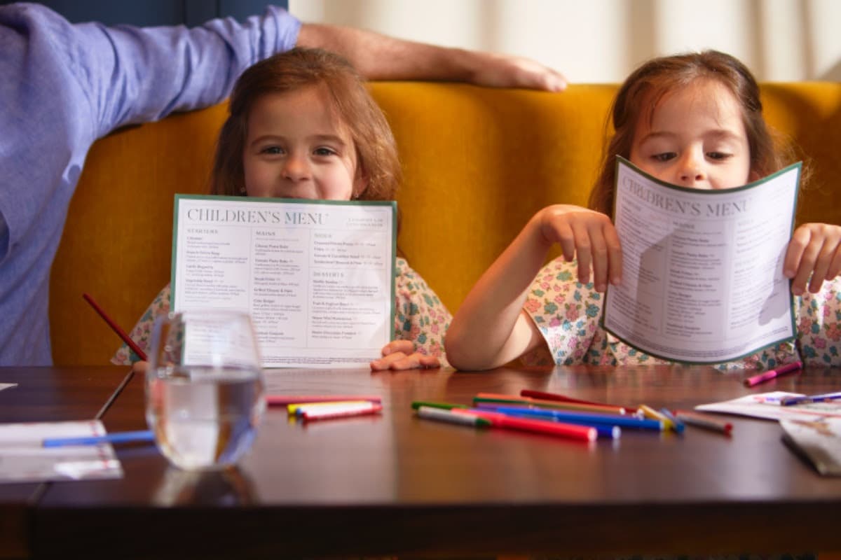 Two young children holding menus at a restaurant table