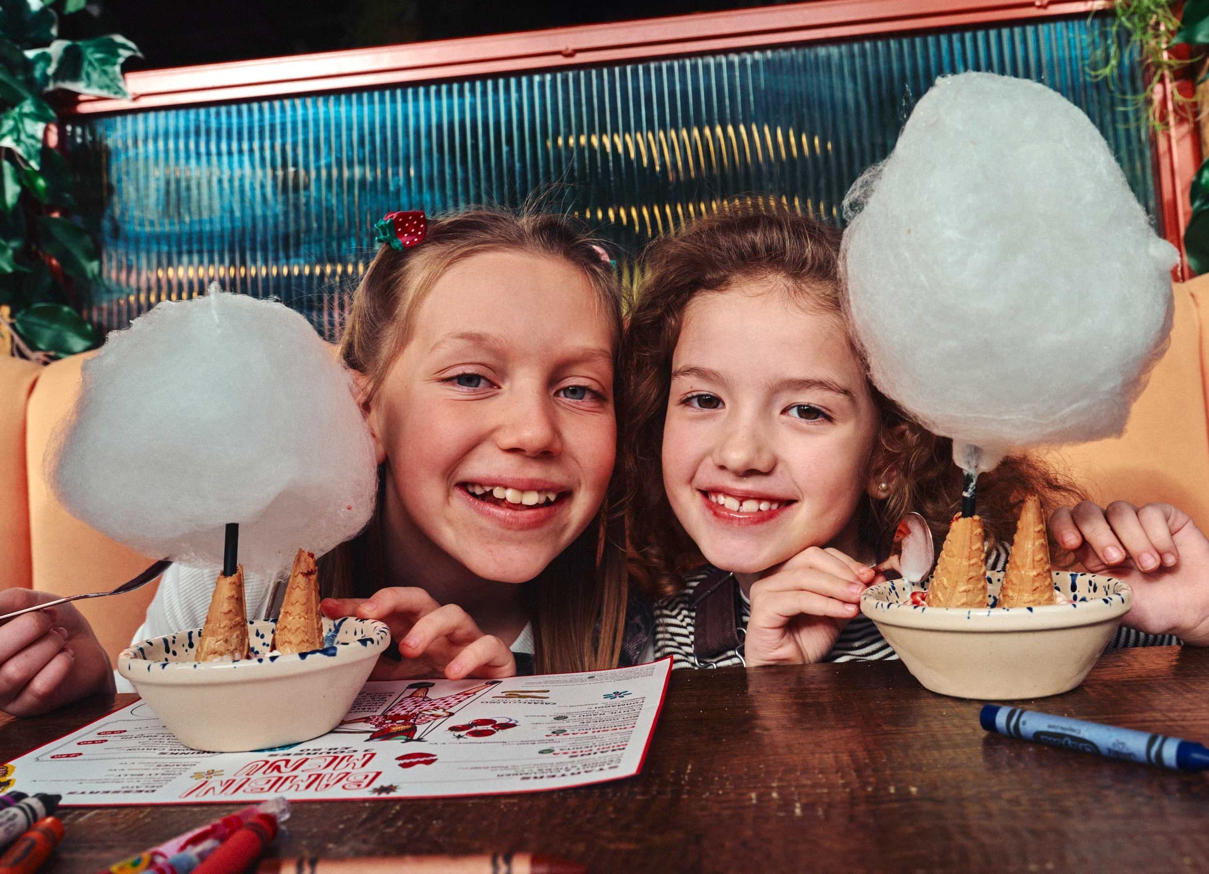 Two smiling children with cotton candy cones in a cafe