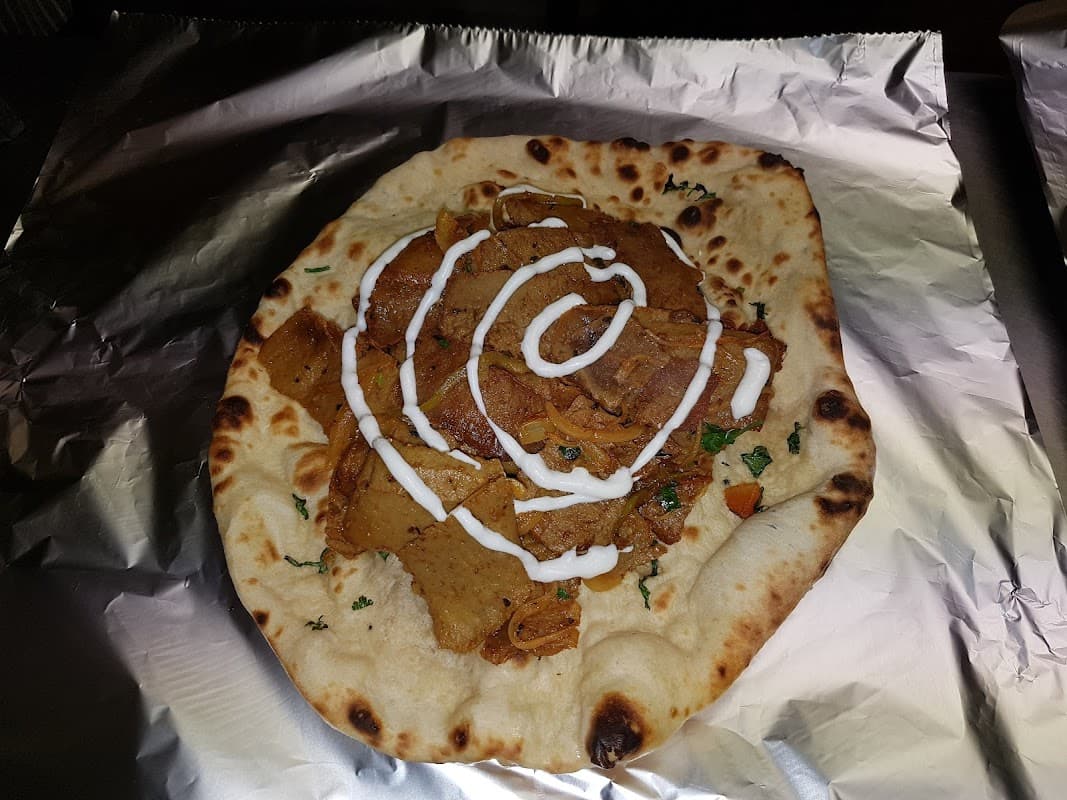 A naan topped with spiced meat, drizzled with yogurt sauce and garnished with herbs, served on foil.