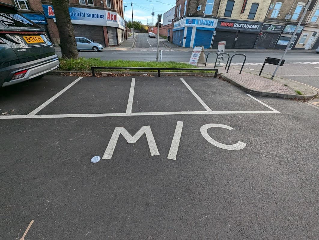 Free parking area with marked spaces, featuring the letters "MIC" on the pavement, near shops in Attercliffe.