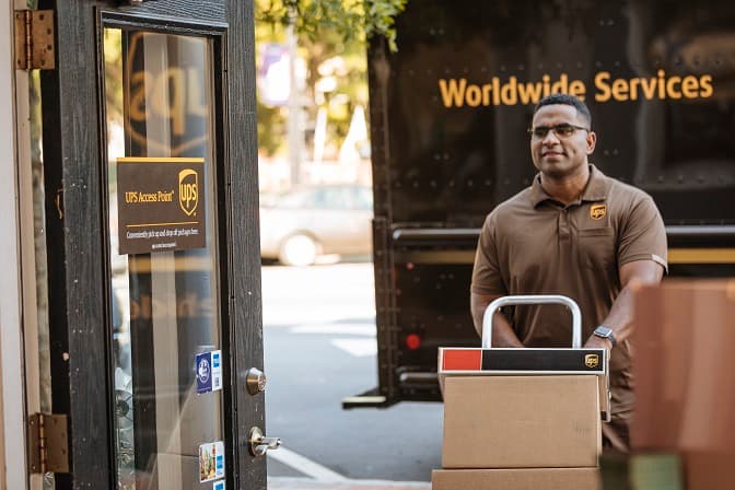 UPS Access Point sign on a door with a delivery person pushing a cart of packages outside.