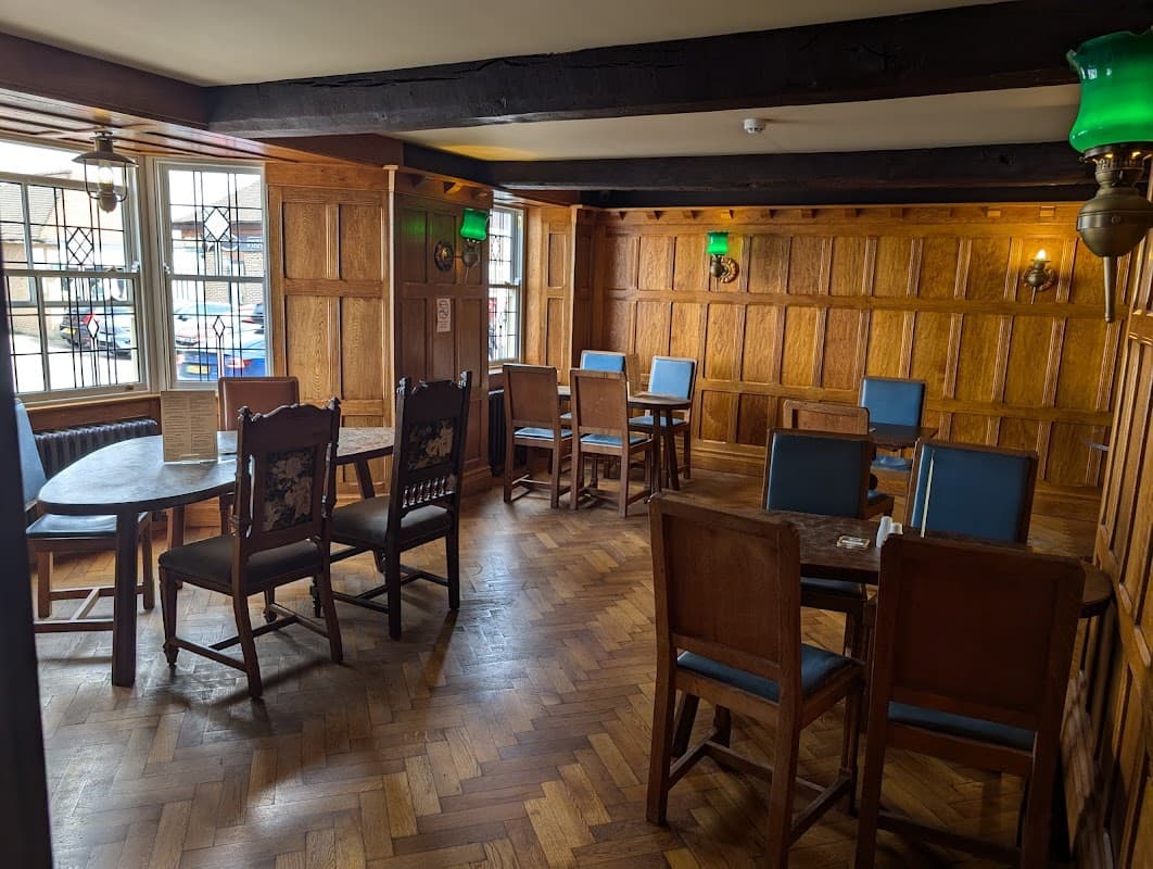 Wooden-paneled bar interior with tables and chairs, green lamps, and a herringbone floor in a cozy atmosphere.