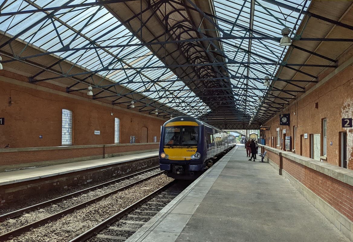 Train arriving at Beverley Railway Station, featuring a brick platform, large windows, and a metal roof structure.