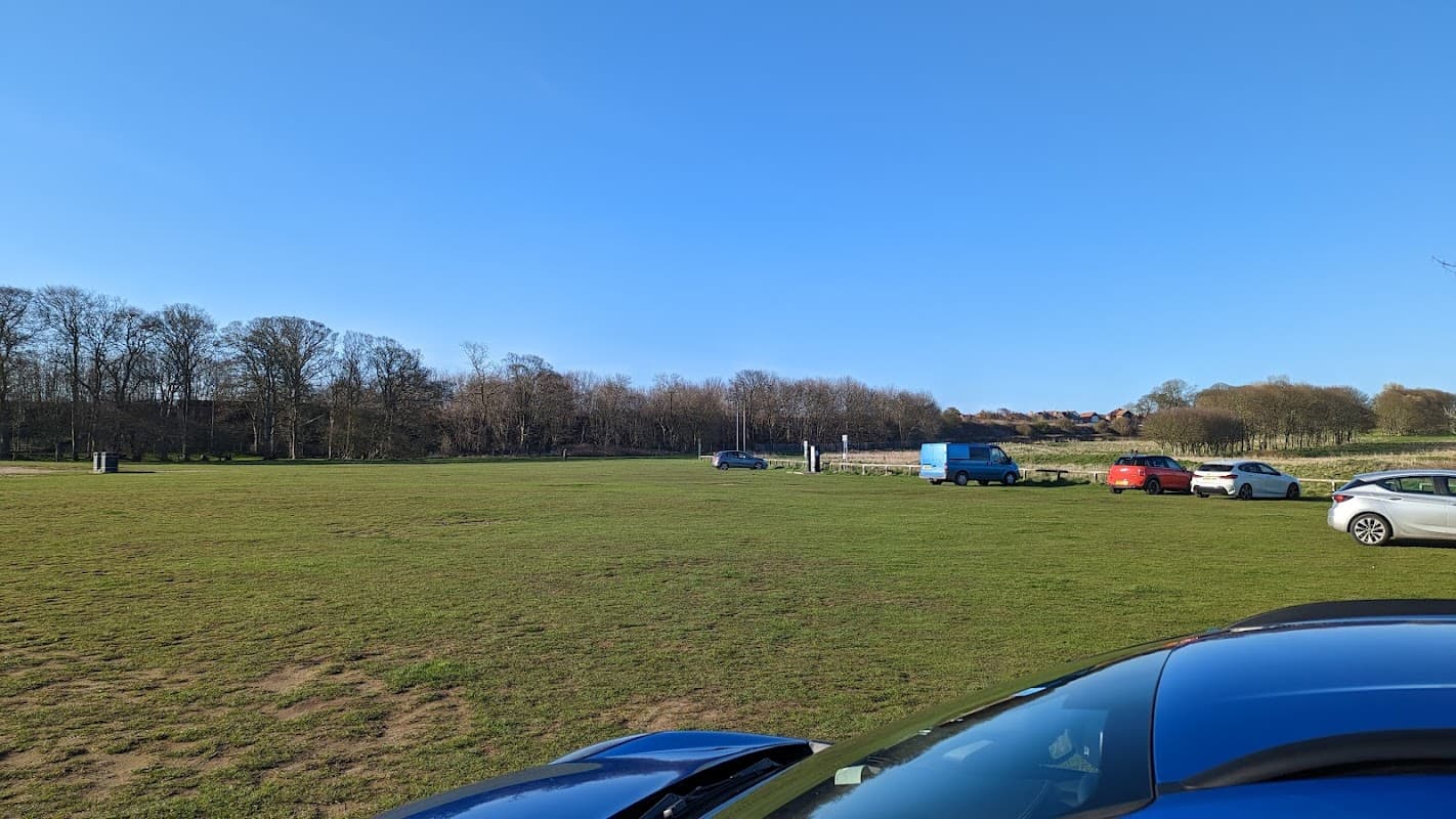 Limekiln Lane Car Park features grassy areas, parked cars, and trees under a clear blue sky in Bridlington, Yorkshire.
