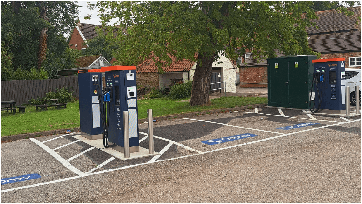 Osprey Charging Station with multiple EV chargers and a green utility box in a parking area, surrounded by trees.