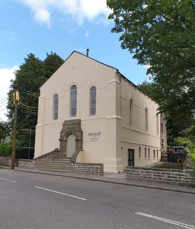 Chapel Gallery Bunkhouse, a light-colored building with large windows, surrounded by trees and a road in Burtersett, Yorkshire.