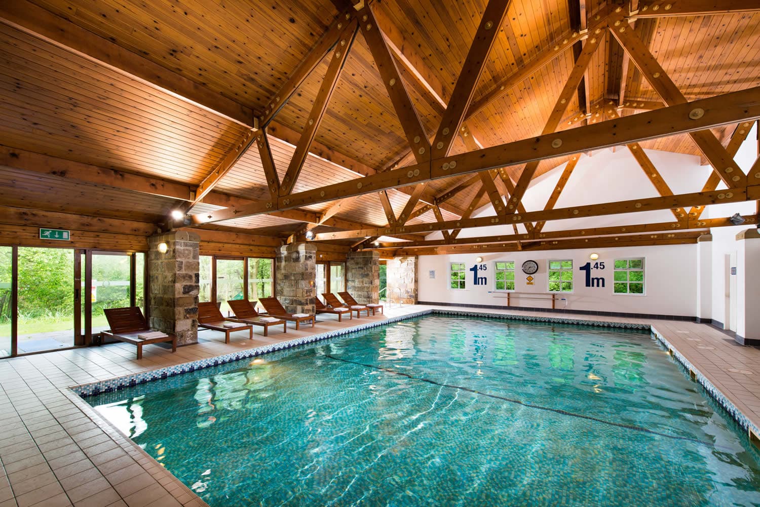 Indoor pool at Chevin Country Park Hotel in Otley, surrounded by wooden beams, lounge chairs, and large windows.