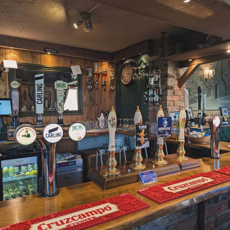 Bar counter with various beer taps, a mirror, and shelves displaying drinks in a rustic setting.