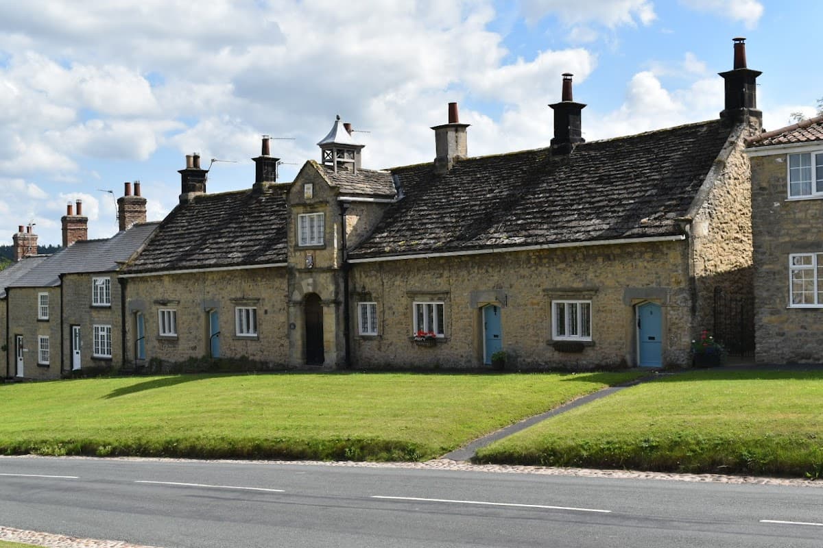 Coxwold Village Hall features a stone faΓ§ade with a central entrance and a clock tower, surrounded by green grass.