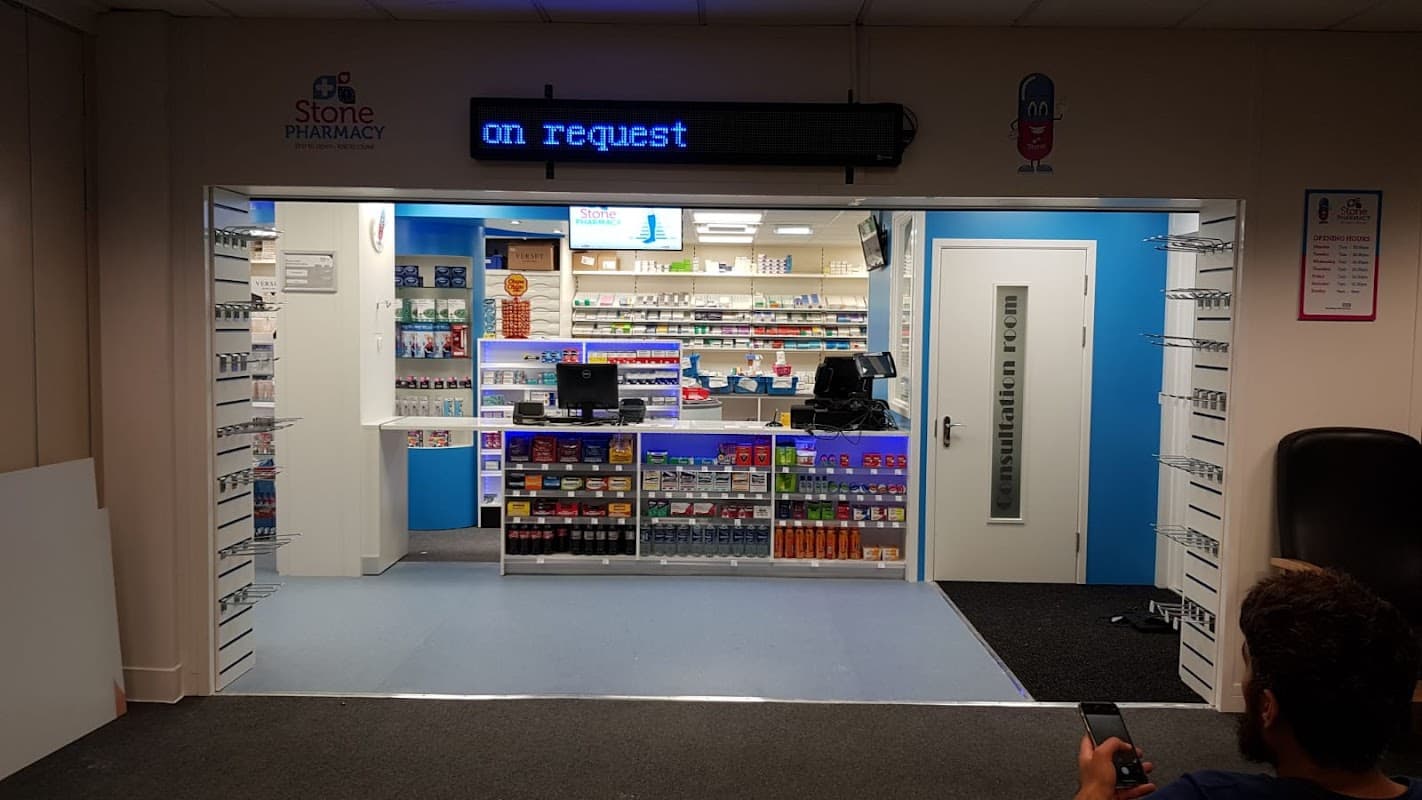 Brightly lit pharmacy entrance with shelves of products, a counter, and a digital sign displaying "on request."