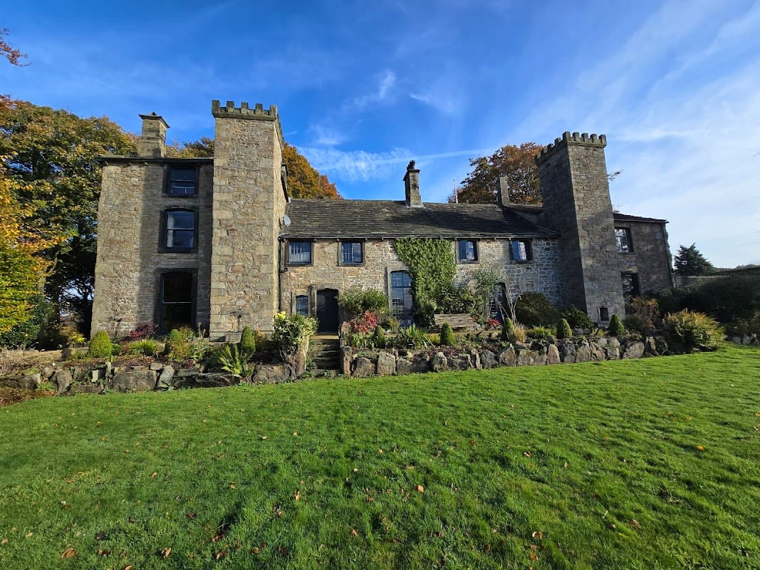 Historic stone building with towers, surrounded by lush greenery and colorful foliage under a bright blue sky.