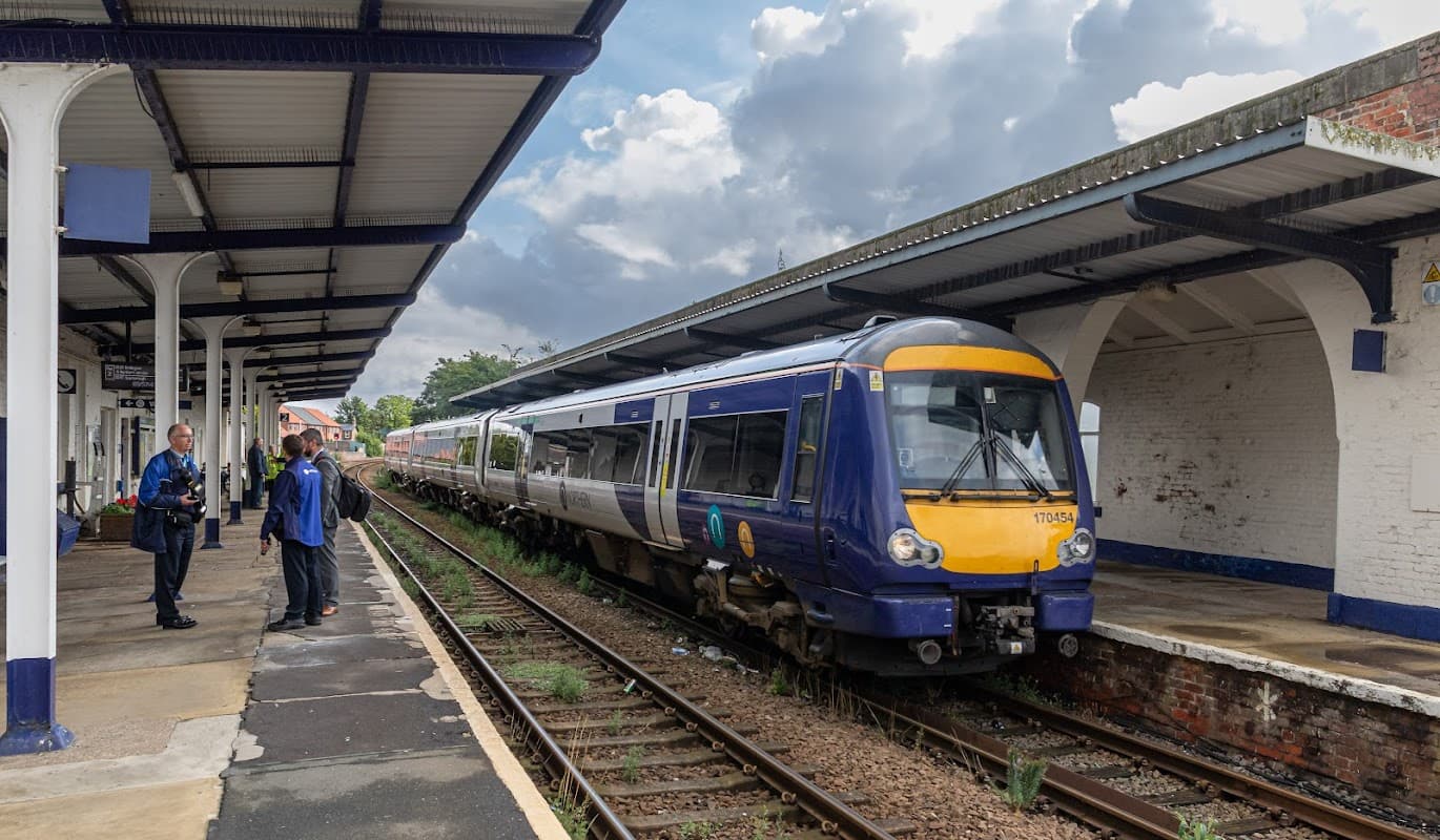 A train at Driffield Railway Station with passengers waiting on the platform under a cloudy sky.