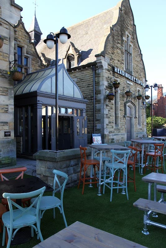 Exterior of The Headingley Taps bar, featuring stylish seating, stone architecture, and a glass entrance.