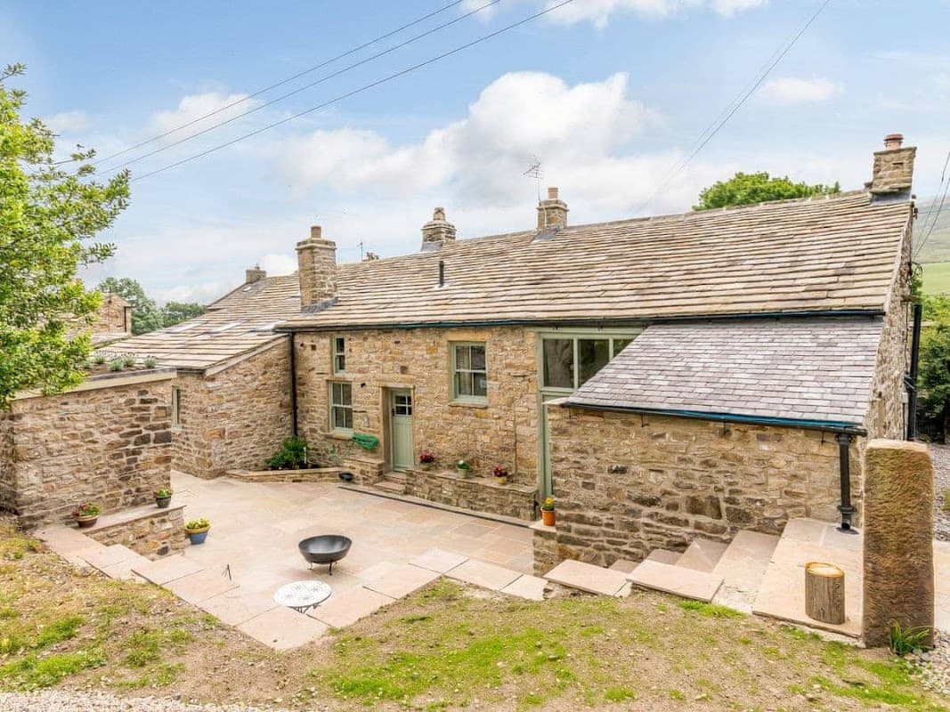 Stone farmhouse with a slate roof, surrounded by greenery and a stone patio, located in a rural Yorkshire setting.