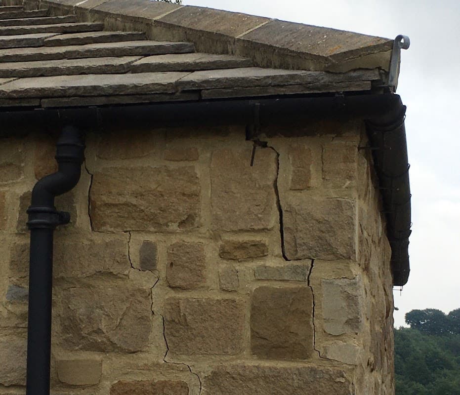 Cracked stone wall with a downpipe, near the roofline of a building in Huby, Yorkshire.
