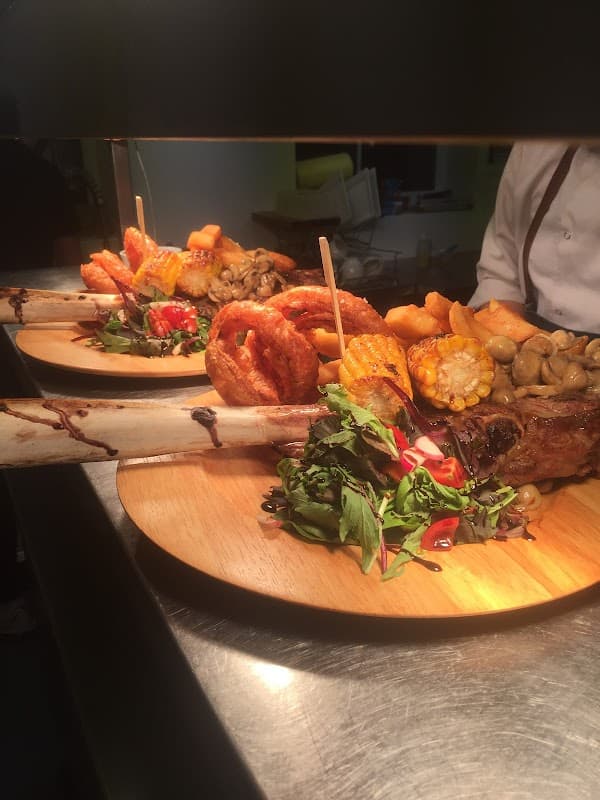 Two beautifully plated dishes featuring grilled meat, roasted vegetables, onion rings, and fresh greens on wooden boards.