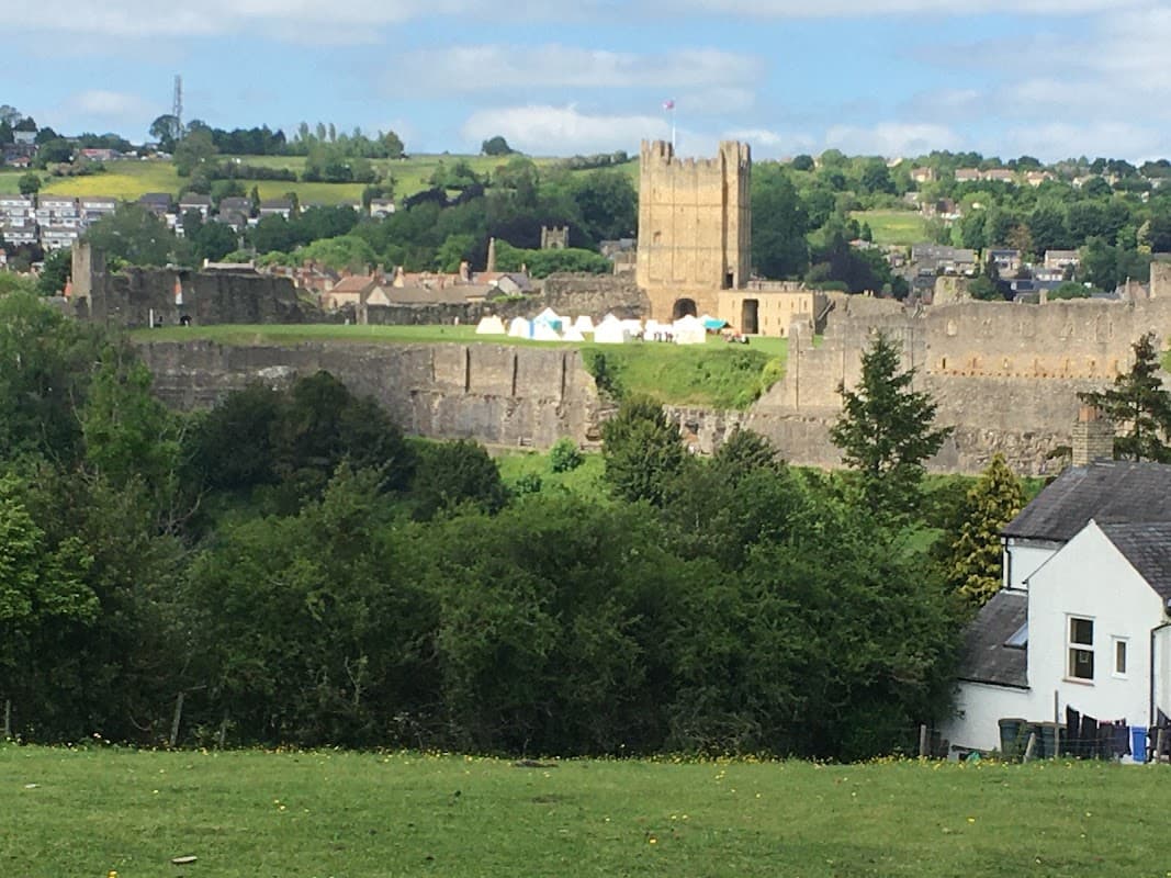 Scar Close Caravan Park with green fields, white tents, and a historic castle tower in the background under a blue sky.
