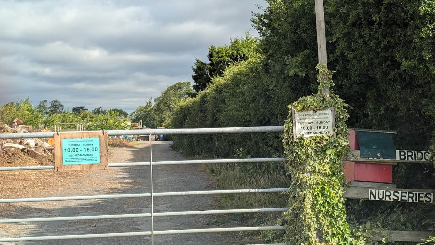 Gated entrance to Hullbridge Nurseries with opening hours signage and lush greenery along the pathway.