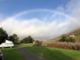 Scenic campsite with a rainbow over rolling hills and a parked campervan