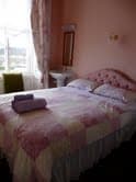 Cozy guest room with pastel decor, double bed, and folded towels on top. Large window with a view in Whitby, Yorkshire.