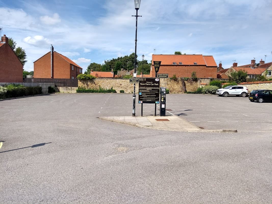 Town Farm Car Park in Kirkbymoorside, featuring a pay station, empty parking spaces, and surrounding residential buildings.