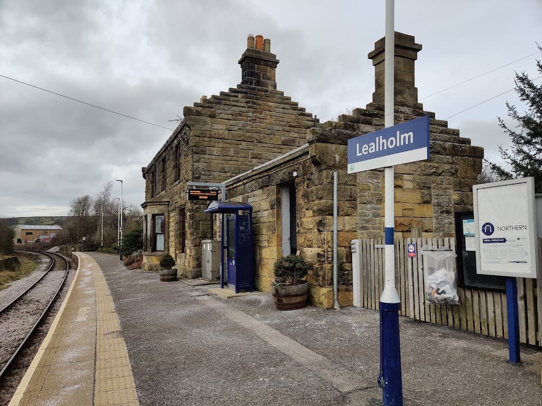 Stone building with a slate roof, sign reading "Lealholm," and a train platform beside railway tracks.
