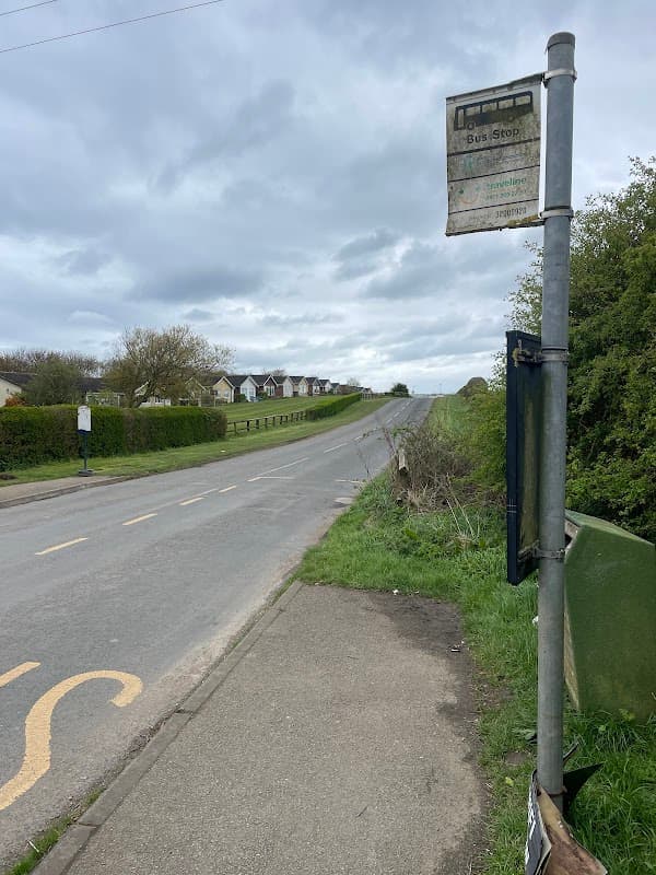 Bus stop sign beside a quiet road in Lebberston, Yorkshire, with houses visible in the distance under a cloudy sky.