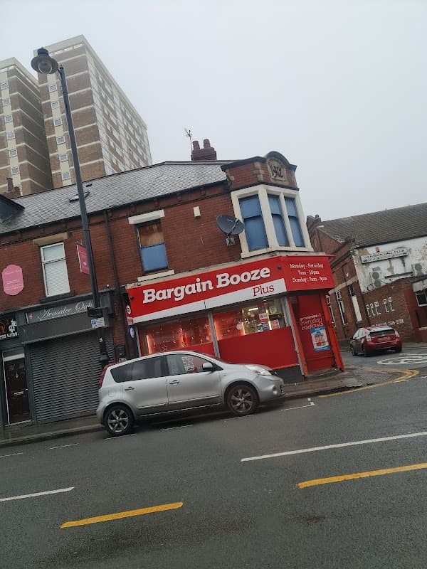 Bargain Booze Plus storefront with red signage, a gray car parked outside, and residential buildings in the background.