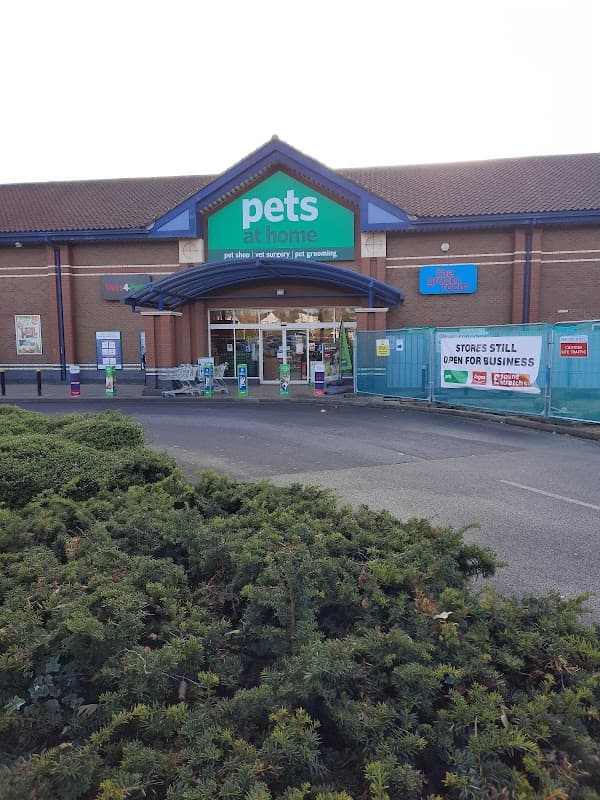 Front entrance of Pets at Home store with signage, surrounded by greenery and construction barriers.