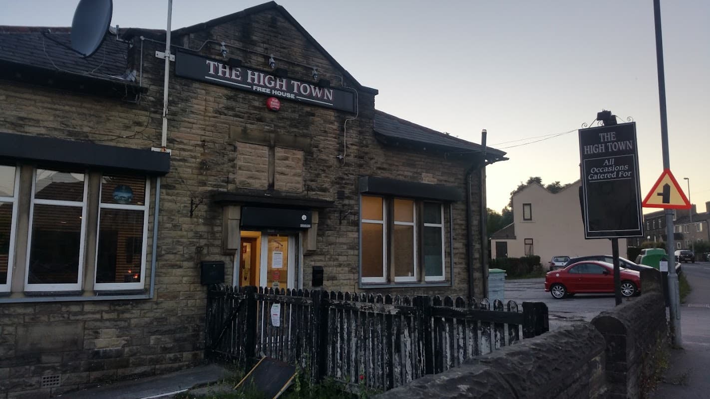 A stone building with large windows, a sign reading "The High Town," and a red car parked nearby.