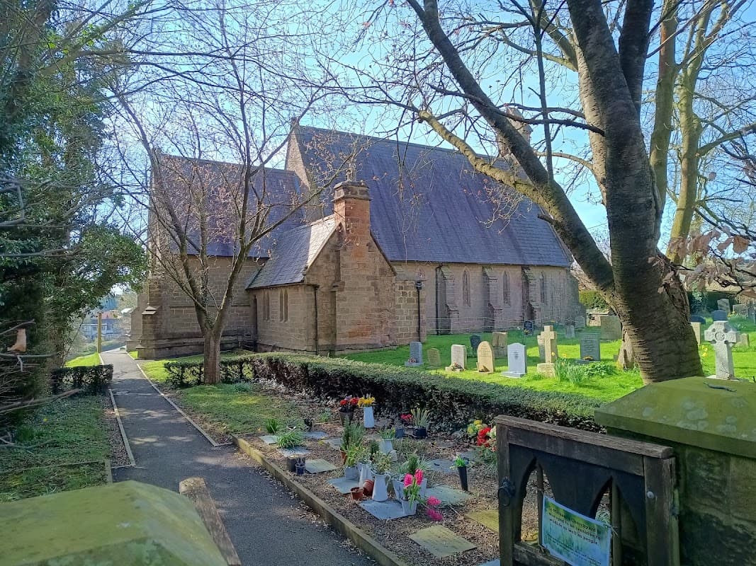 St. Michael Markington church surrounded by trees and a graveyard with flowers in Markington, Yorkshire.