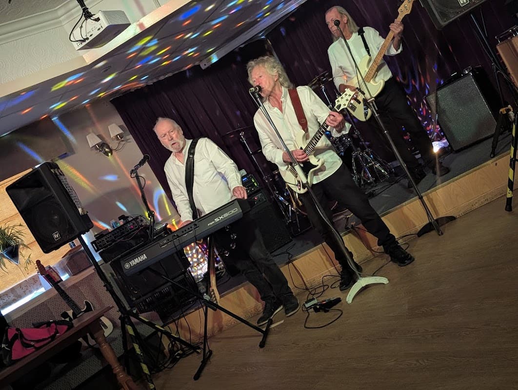 Live band performing at Meltham Liberal Club, with colorful lights and musical instruments on stage.