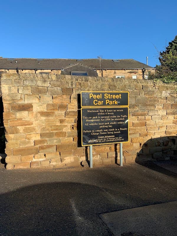 Sign for Peel Street Car Park with stone wall background, detailing parking rules and payment instructions.