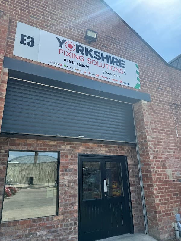 Sign for Yorkshire Fixing Solutions Ltd above a large black roller shutter door on a brick building.