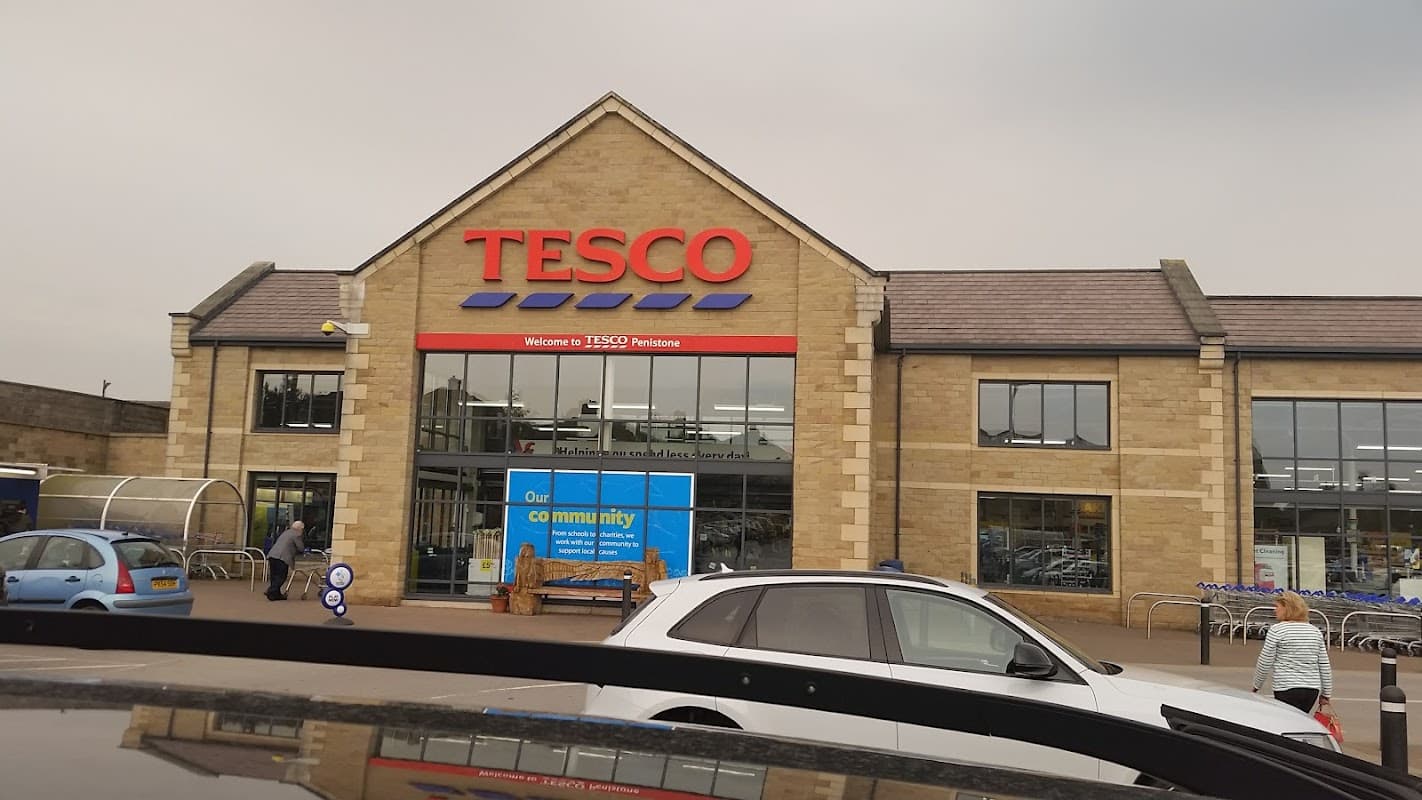 Tesco Superstore in Penistone, Yorkshire, featuring a stone facade and large windows, with parked cars in front.