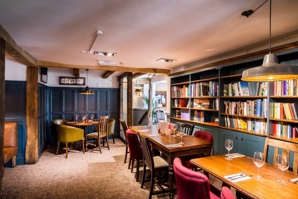 Cozy bar interior with wooden beams, bookshelves, and tables set for dining in Plompton, Yorkshire.