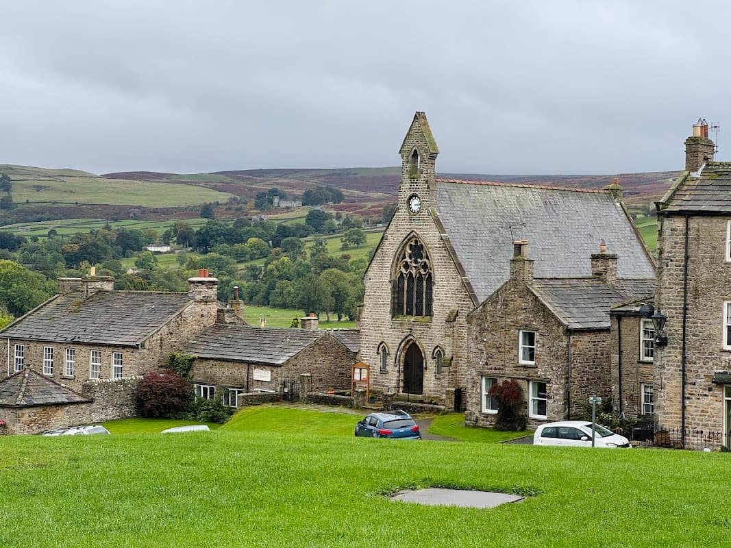 Swaledale Museum features a stone building with a clock tower, surrounded by green fields and traditional Yorkshire houses.
